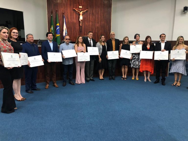 #PraCegoVer #DescriçãoDaImagem Foto de 14 Representantes das Instituições. Há 6 mulheres e 8 homens,  as pessoas estão lado a lado, formando um semicírculo e estão em frente à mesa de solenidade. Todos seguram o Certificado de homenagem. Klaiton, o homenageado membro do Retina Ceará, está de blusa social azul, usando óculos escuro. Ele está entre os homenageados na quinta posição da esquerda para a direita.