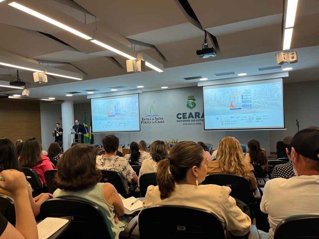 Auditório do Congresso fotografo de trás, com pessoas sentadas de costas e, ao fundo, dois telões com projeções